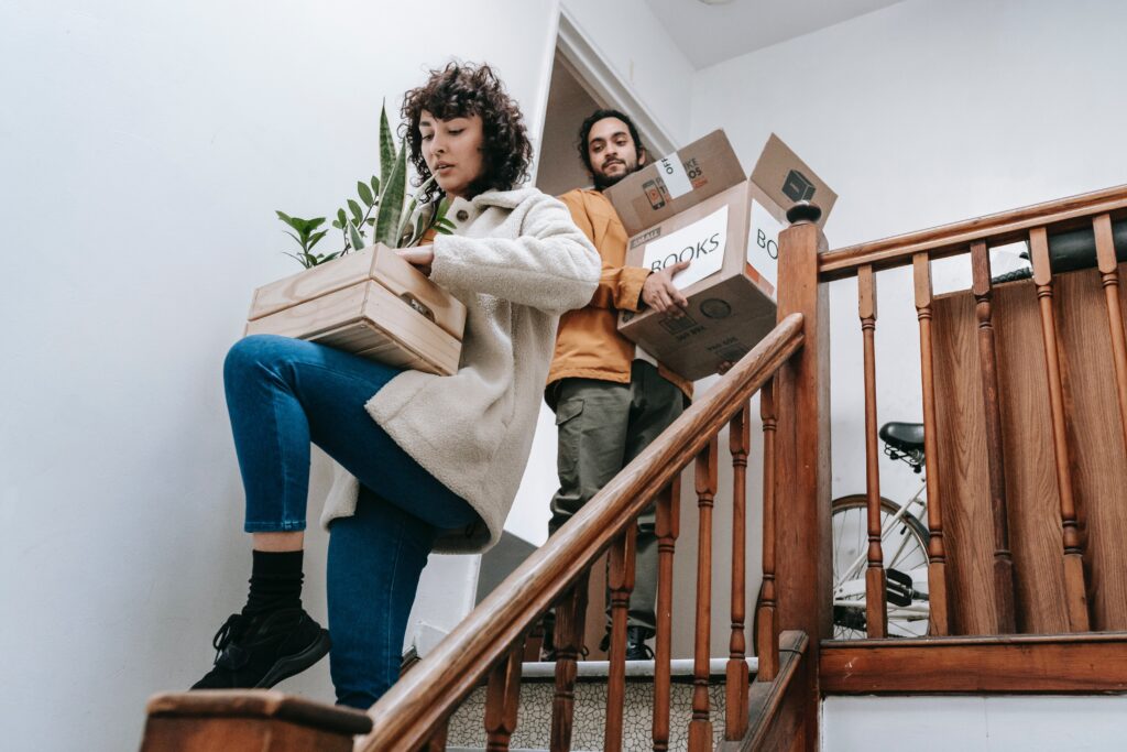 Two people carrying boxes down stairs.